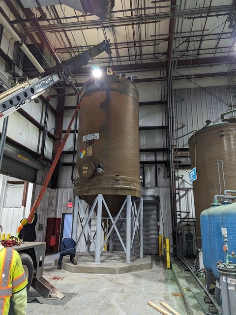 Crane lowering a large storage tank into place inside an industrial facility